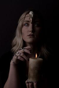 Portrait of spooky woman holding lit candle against black background