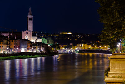 Illuminated buildings by river against sky at night