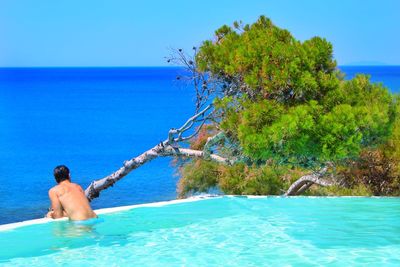 Full length of shirtless man in swimming pool against sea