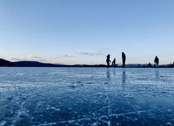 People on frozen lake against blue sky during winter