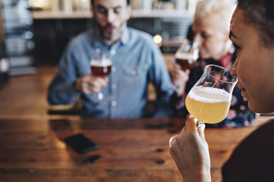 Close-up of woman examining craft beer while sitting with friends at bar