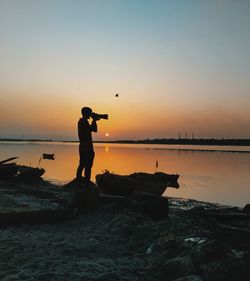 Silhouette man standing on rock by sea against sky during sunset