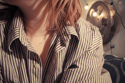 Midsection of woman wearing striped button down shirt in illuminated room