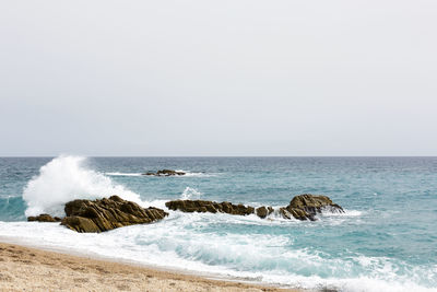 Scenic view of wave splashing on a rock against clear sky