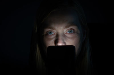 Close-up portrait of woman using phone in dark