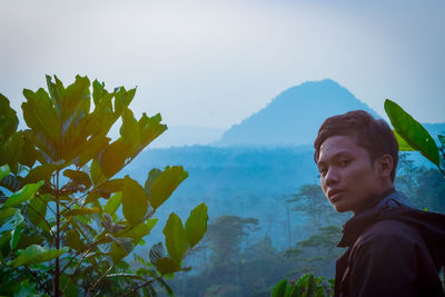 Portrait of young man looking at mountains against sky