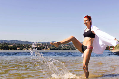 Playful woman having fun in summer day and splashing water at the beach.