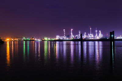 Illuminated city by sea against sky at night