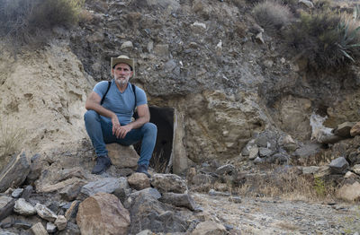 Portrait of adult man in cowboy hat and jean sitting in a rural area