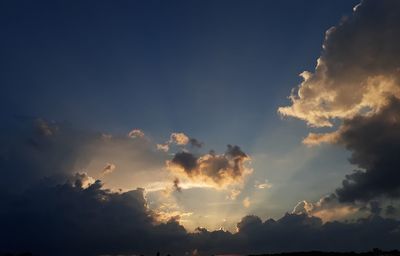 Low angle view of sunlight streaming through clouds during sunset