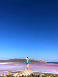 Woman standing on beach against clear blue sky