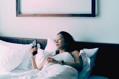 Young woman using mobile phone while lying in bed at home