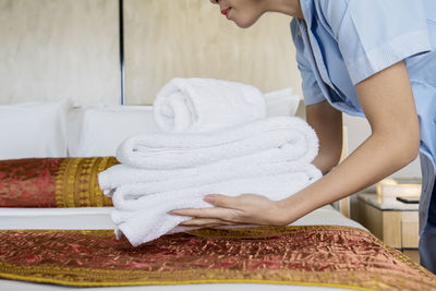 Midsection of young woman placing laundry on bed at home