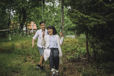 Boy pushing grandmother on swing near trees in garden