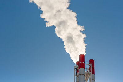 Factory metallic chimney with white steam or smoke against a blue sky.