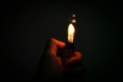 Close-up of hand holding lit candle against black background