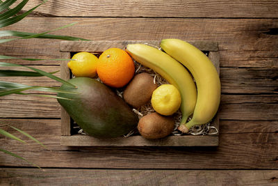 Fresh tropical fruits in a wooden delivery box on a wooden background. orange, banana, mango, kiwi