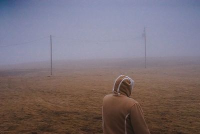 Rear view of woman in warm clothing standing on field during foggy weather