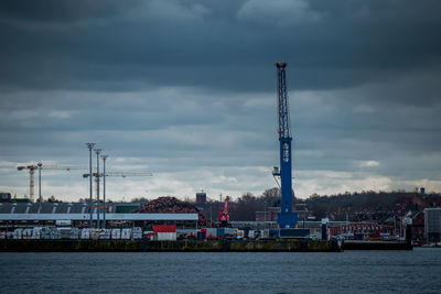 Cranes at harbor against sky