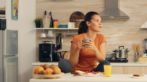 Woman looking away while having coffee in kitchen at home