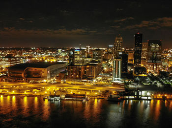 Illuminated buildings by river against sky at night