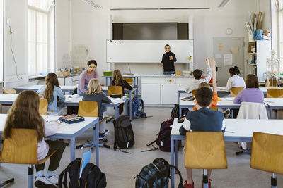 Male and female teacher teaching students sitting on bench in classroom