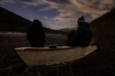 Rear view of two people sitting on riverbank