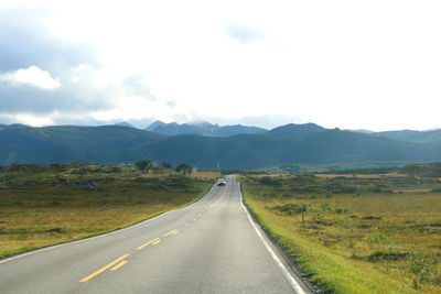 Empty road leading towards mountains against sky