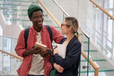 Two happy diverse students standing in university corridor talking communicating during break