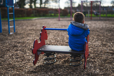 The back of a small boy playing alone in a park looking sad that he is playing alone