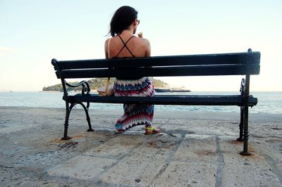 Rear view of woman sitting on bench at beach