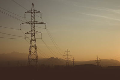 Low angle view of silhouette electricity pylons against clear sky