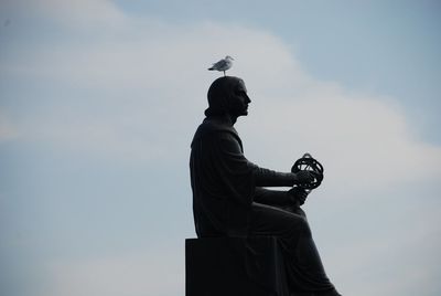 Low angle view of seagull perching on statue against sky