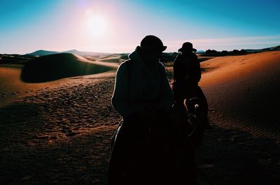 Silhouette men on camels at desert against sky