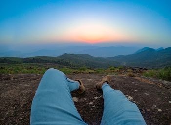 Low section of person on land against sky during sunset