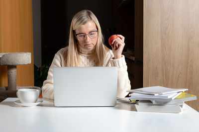 Mid adult woman using smart phone while sitting on table