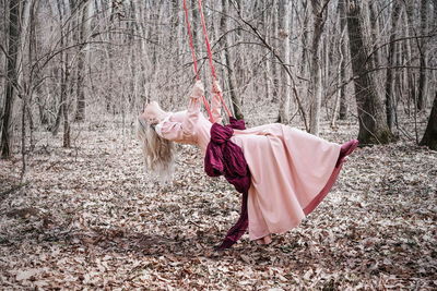 Woman swinging in swing by bare trees in forest