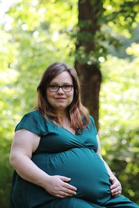 Portrait of pregnant woman sitting against trees