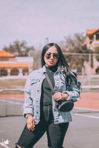 Young woman wearing sunglasses standing against sky