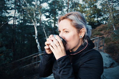 Close-up of woman having drink while standing against trees