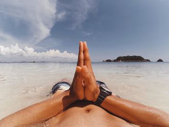 Midsection of man with hands clasped lying on shore at beach against sky