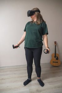 A girl in a virtual reality helmet with controllers in her hands stands in a gray room