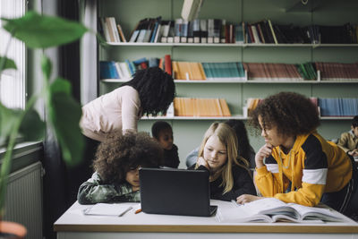 Multiracial students watching laptop while studying in classroom