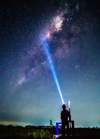 Rear view of man standing on land against sky at night