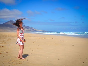Woman tossing hair while standing on sand at beach against sky