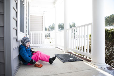 Wide view of boy in pink snow pants sitting on snowy front porch