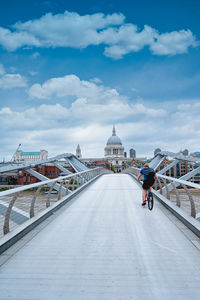 People riding bicycle on bridge in city against sky