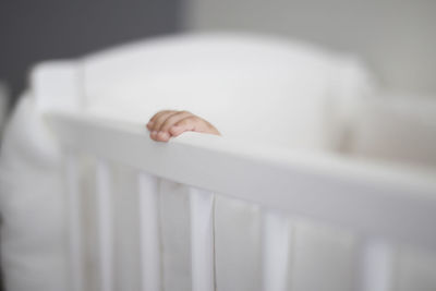 Cropped hand of baby in white crib at home