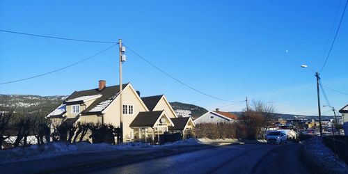 Road by buildings against clear blue sky in city