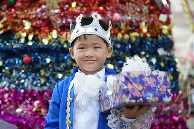 Smiling boy wearing crown holding gift box while standing in party